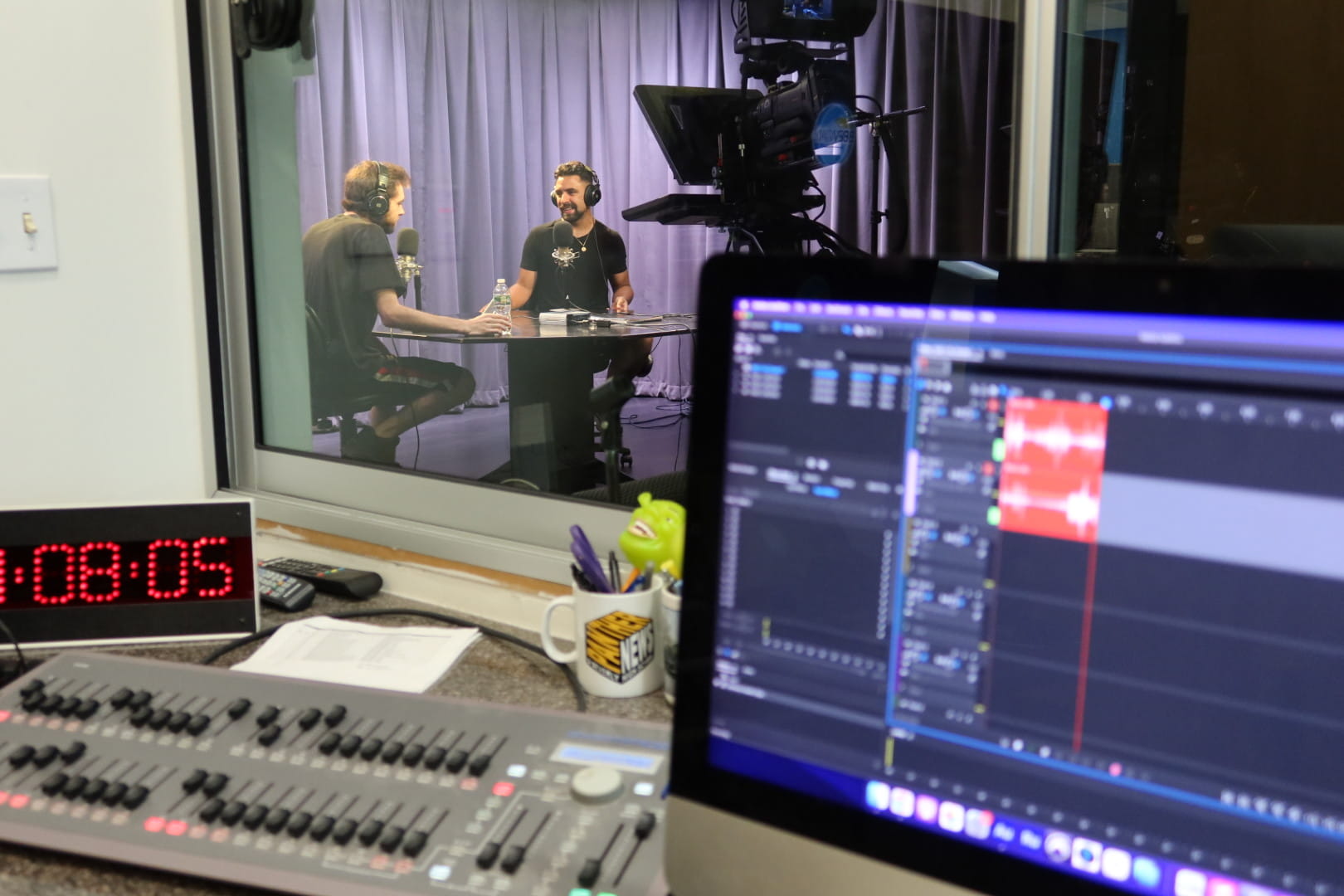 View from the control room of two bearded men in a podcast studio.